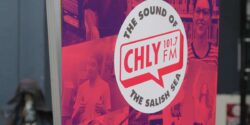 Photo of large promotional banner that has red-tinted photos surrounding the phrase: The Sound of CHLY 101.7 FM The Salish Sea. Photo by J. Waits