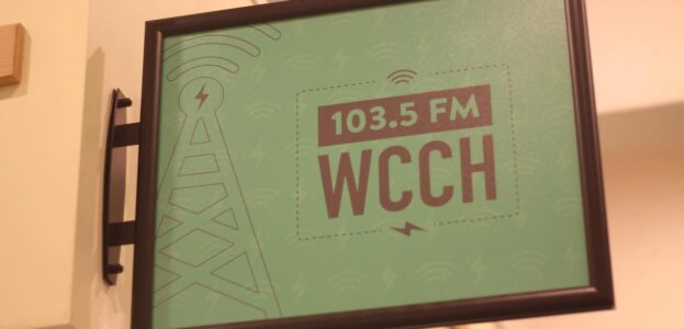 Photo of green sign attached to a wall that reads 103.5 FM WCCH at the Holyoke Community College radio station. Photo: J. Waits